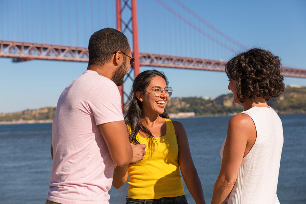 Grupo de amigos felizes a socializar ao ar livre com a Ponte 25 de Abril em Lisboa ao fundo