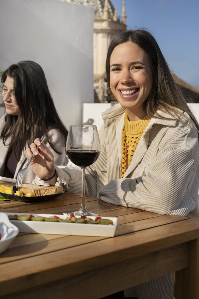 Duas amigas sorridentes a desfrutar de um copo de vinho numa esplanada ao ar livre